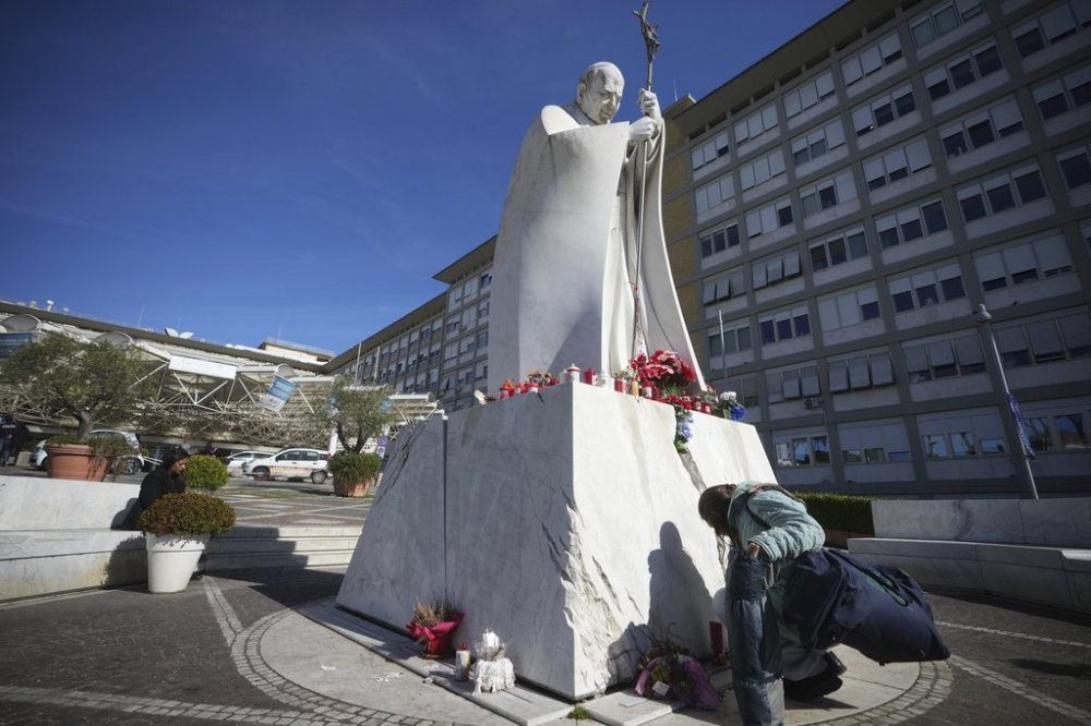A woman kneels at the foot of a statue of late Pope John Paul II outside the Agostino Gemelli Polyclinic in Rome, Sunday, Feb. 16, 2025, where Pope Francis was hospitalised Friday after a week-long bout of bronchitis worsened and is receiving drug therapy for a respiratory tract infection that made impossible for him to attend the traditional Sunday public blessing after the noon Angelus prayer. (AP Photo/Alessandra Tarantino)