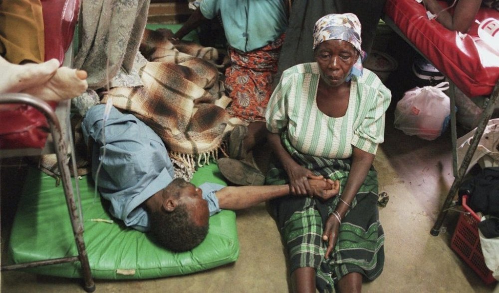 FILE - A woman holds the hand of a sick relative lying on the floor of the overcrowded Lilongwe Central Hospital, in Lilongwe, Malawi, Sept. 30, 1998, as the hospital is overflowing because of an epidemic of AIDS rampaging in southern Africa. (AP Photo /Denis Farrell, File)