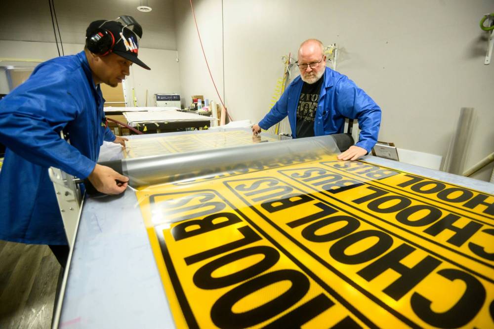 MIKE SUDOMA / FREE PRESS
Louie De Ala (left) and Forrest Buchannon work together to laminate a stack of school bus signage.