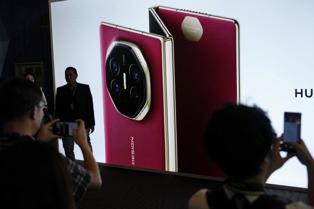 Visitors take pictures in-front of a giant billboard display of Huawei's industry's first tri-foldable phone during the opening of its global sales in Kuala Lumpur, Malaysia, Tuesday, Feb. 18, 2025. (AP Photo/Vincent Thian)
