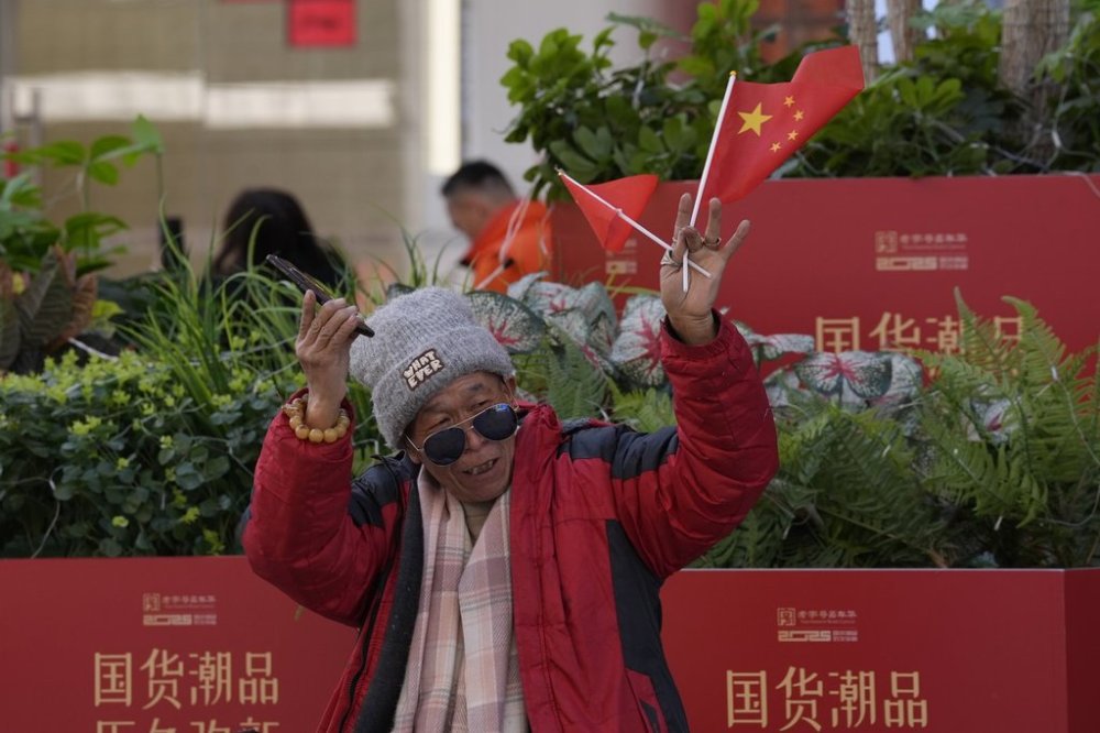 A man waves the Chinese national flag and Communist Party flag in the popular Wangfujing shopping street in Beijing, China, Thursday, March 6, 2025. (AP Photo/Ng Han Guan)