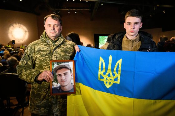 Former Ukrainian soldier Betro Lukin holds a framed image of his late son, Nazanir, while his younger son, Kiril, holds up a Ukrainian flag during a ceremony marking the third anniversary of Russia‘s invasion of Ukraine at the Canadian Museum for Human Rights Sunday. (Mike Sudoma / Free Press)