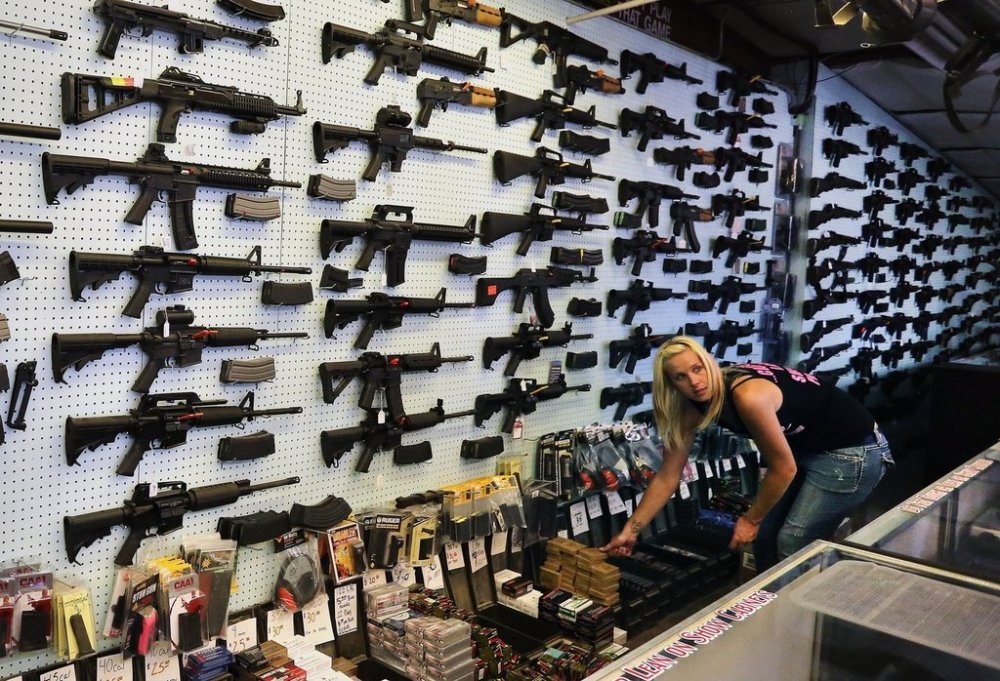 FILE - In this July 20, 2014 photo, with guns displayed for sale behind her, a gun store employee helps a customer at Dragonman's, east of Colorado Springs, Colo. (AP Photo/Brennan Linsley, File)