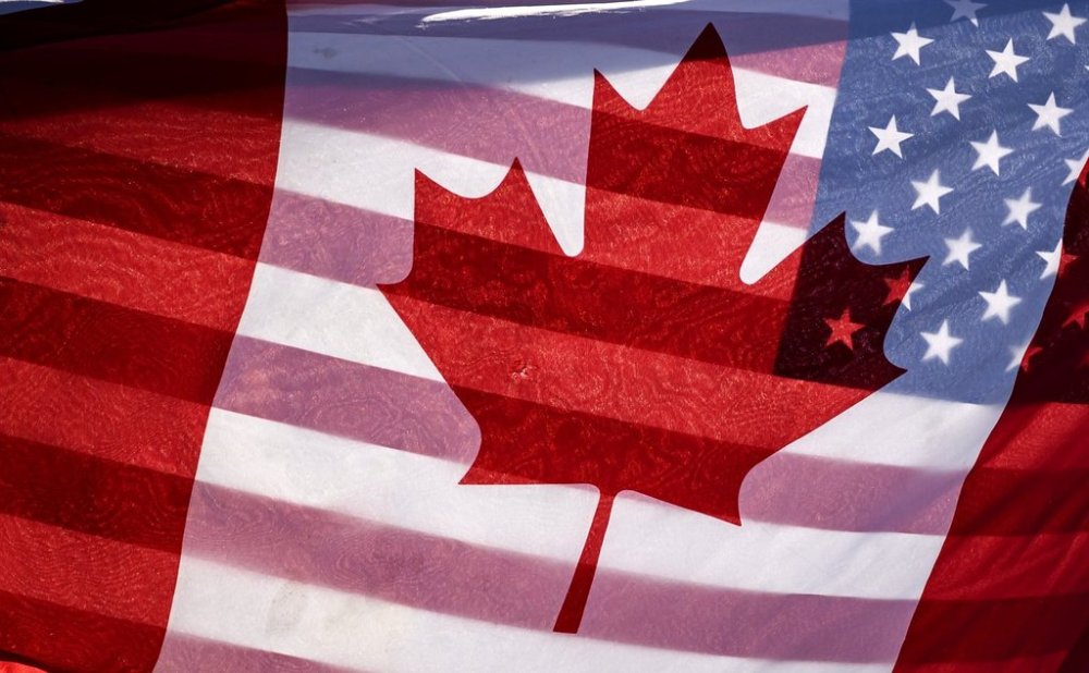 Sunlight shines through the flags of Canada and the United States, held together by a protester outside on Parliament Hill in Ottawa, Saturday, Feb. 1, 2025. THE CANADIAN PRESS/Justin Tang