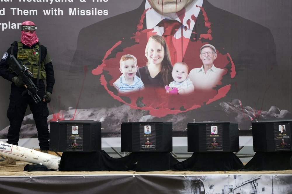 A militant stands next to the coffins containing the bodies of hostages, from right to left, Shiri Bibas, her two children, Ariel and Kfir and Oded Lifshitz, who was 83 when he was abducted before their are handed over to the Red Cross in Khan Younis, southern Gaza Strip, Thursday, Feb. 20, 2025. (AP Photo/Abdel Kareem Hana)