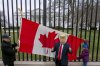 Toronto residents Douglas Bloomfield, left, and his son Phoenix, right, who are on vacation in Washington, hold a Canadian flag and an ice hockey stick to show their support for Canada regarding trade tariffs as they pose with with another visitor to the city wearing a mask of President Donald Trump in front of the White House in Washington, Thursday, March 13, 2025. (AP Photo/Ben Curtis)