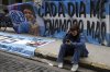 A fan of the late soccer star Diego Maradona sits near a flag with his image that reads in Spanish 