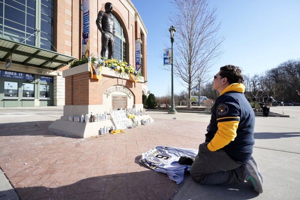 A fan kneels in front of the Bob Uecker statue outside American Family Field following a baseball game between the Milwaukee Brewers and the Kansas City Royals on Opening Day, Monday, March 31, 2025, in Milwaukee. (AP Photo/Kayla Wolf)