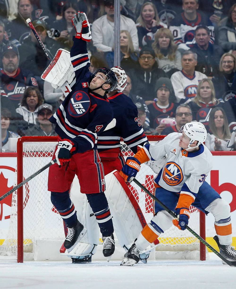 Winnipeg Jets’ Neal Pionk (4) reaches up to clear the puck as he defends against New York Islanders’ Kyle MacLean (32) during second period NHL action in Winnipeg February 7. (John Woods / The Canadian Press files)