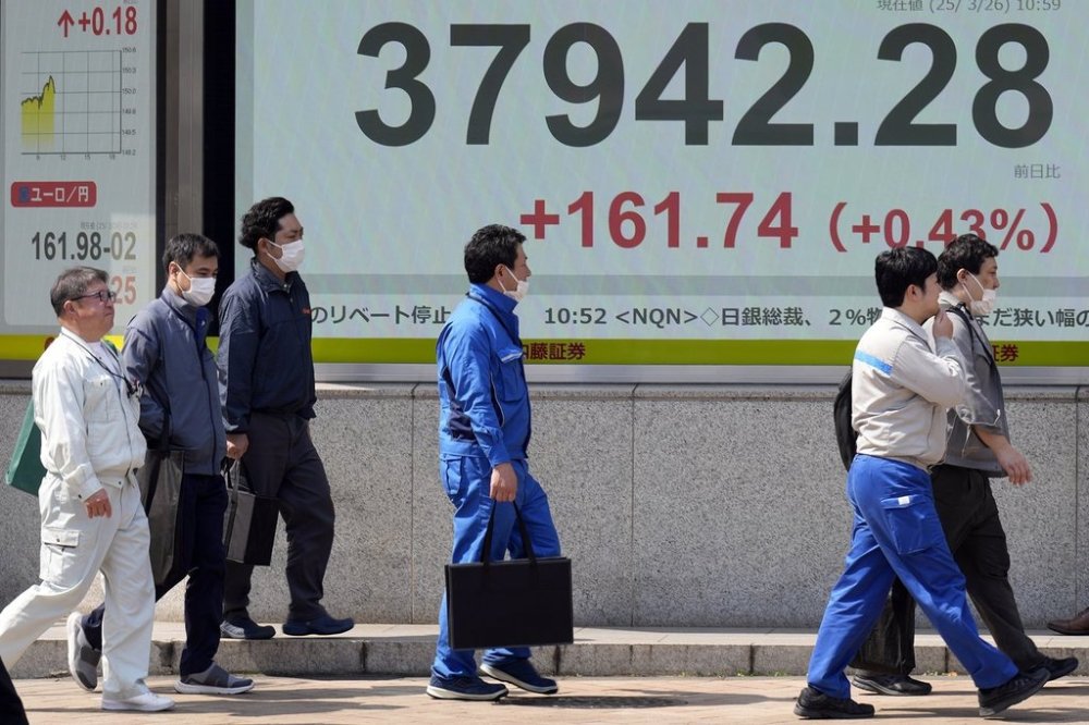 People walk in front of an electronic stock board showing Japan's Nikkei index at a securities firm Wednesday, March 26, 2025, in Tokyo. (AP Photo/Eugene Hoshiko)