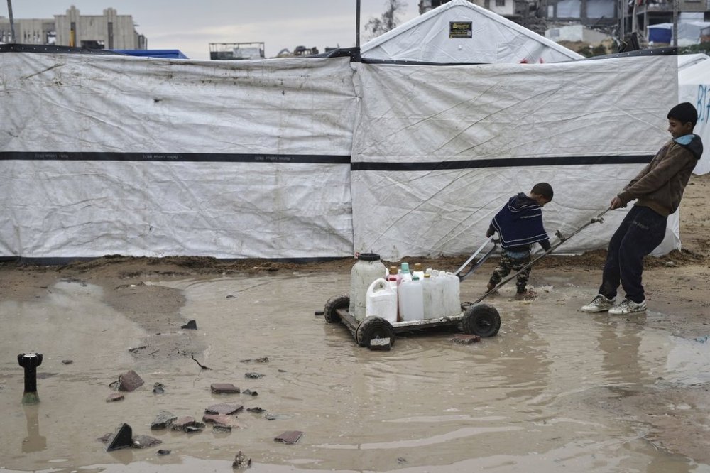 A boy and a child carry water in plastic jerrycans at a tent camp for displaced Palestinians whose homes were damaged by Israeli army strikes in the Zeitoun neighborhood of Gaza City, Friday, March 7, 2025. (AP Photo/Jehad Alshrafi)