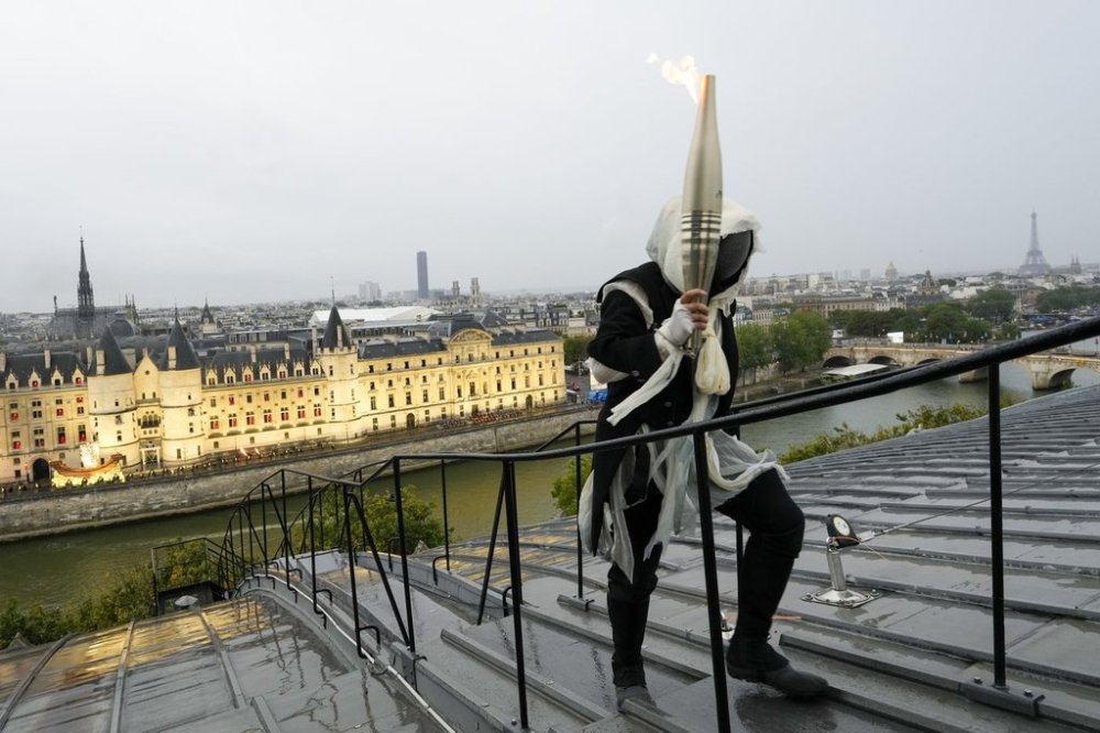 FILE - A torchbearer carries the Olympic flame over a building along the Seine River in Paris, France, during the opening ceremony for the 2024 Summer Olympics, July 26, 2024. (AP Photo/Bernat Armangue, Pool, File)