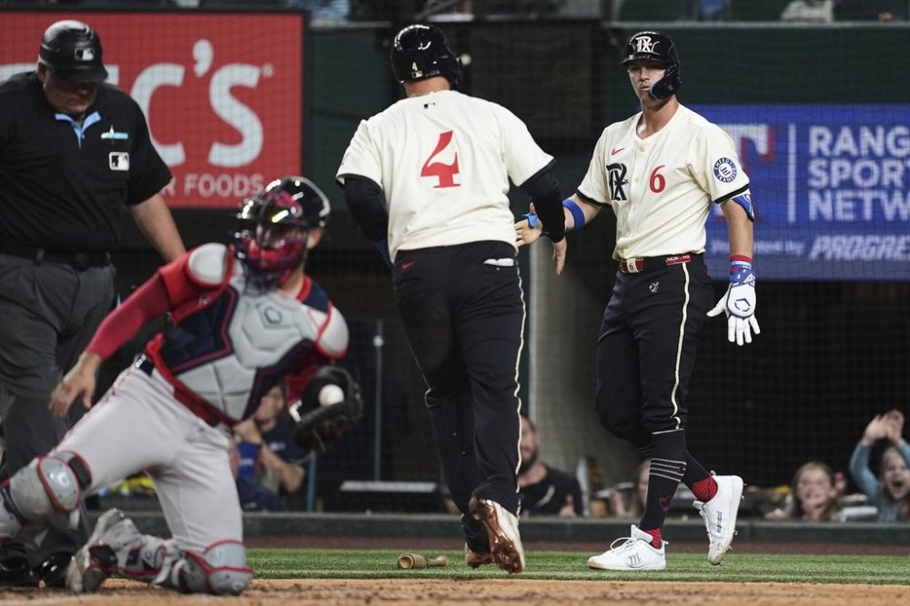 Texas Rangers' Joc Pederson (4) and Josh Jung (6) celebrate after Pederson scored on a Jake Burger double as Boston Red Sox's Connor Wong, second from left, holds the ball by the plate in the sixth inning of a baseball game, Friday, March 28, 2025, in Arlington, Texas. (AP Photo/Tony Gutierrez)