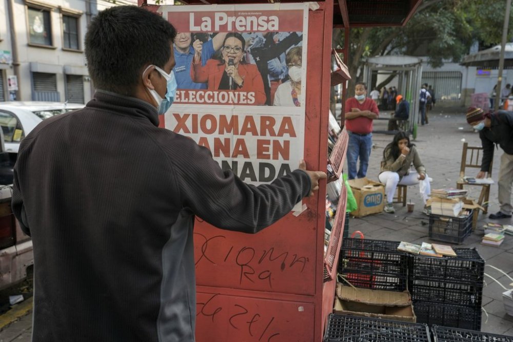FILE - A man hangS a poster with a photo of presidential candidate Xiomara Castro and the day's headline of her expected victory at his newspaper stand after general elections in Tegucigalpa, Honduras, Nov. 29, 2021. (AP Photo/Moises Castillo, File)