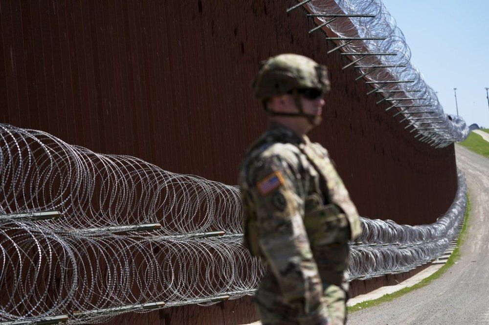 FILE - A member of the military looks on in front of newly-installed concertina wire lining one of two border walls separating Mexico from the United States during a news conference on joint operations involving the military and the Border Patrol, March 21, 2025, in San Diego. (AP Photo/Gregory Bull, File)