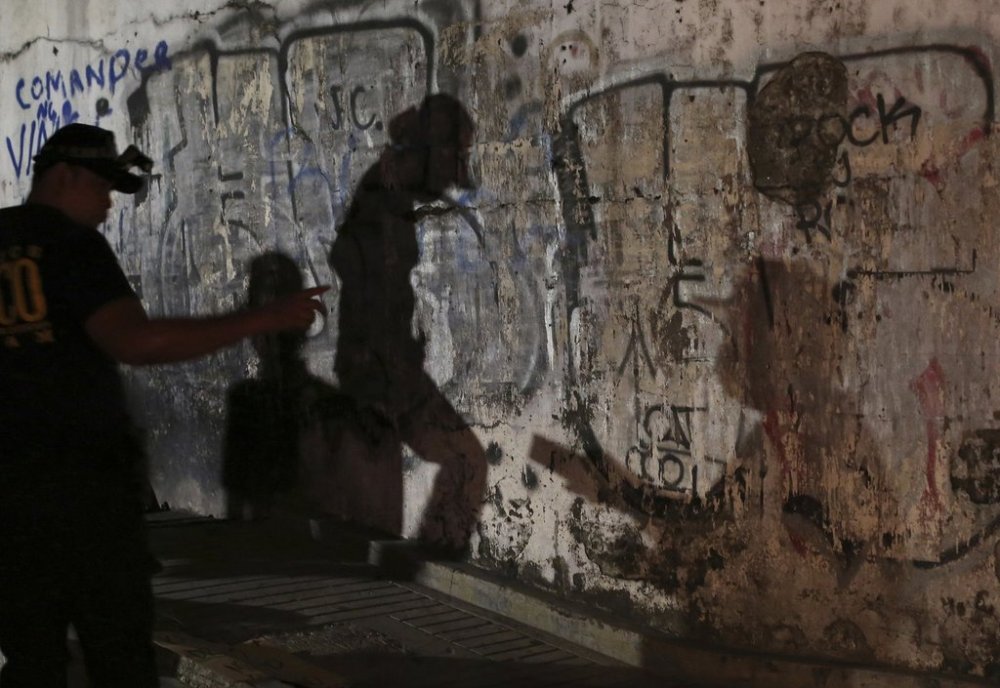 FILE - The shadows of police investigators are reflected on a wall as they check an unidentified body of an alleged drug lord after it was dumped along a dark alley in Manila, Philippines, Sept. 21, 2016. (AP Photo/Aaron Favila, File)