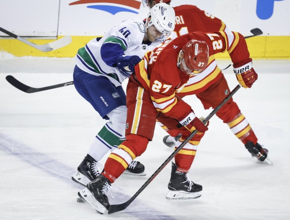 Vancouver Canucks' Elias Pettersson, left, checks Calgary Flames' Matthew Coronato during second period NHL hockey action in Calgary, Alta., Wednesday, March 12, 2025. THE CANADIAN PRESS/Jeff McIntosh