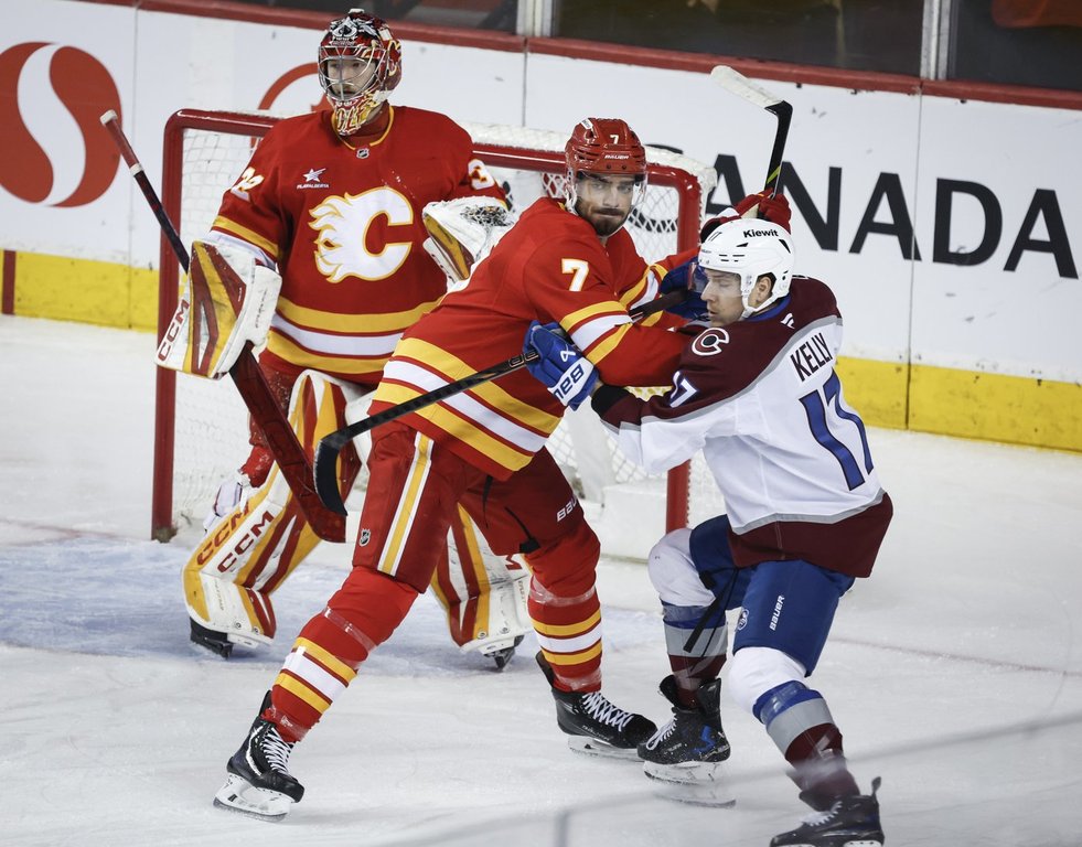 Colorado Avalanche's Parker Kelly, right, is checked by Calgary Flames' Kevin Bahl, centre, as goalie Dustin Wolf follows the play during first period NHL hockey action in Calgary on Friday, March 14, 2025.THE CANADIAN PRESS/Jeff McIntosh