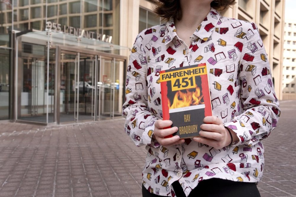 A person wearing a shirt covered in books holds a copy of the novel