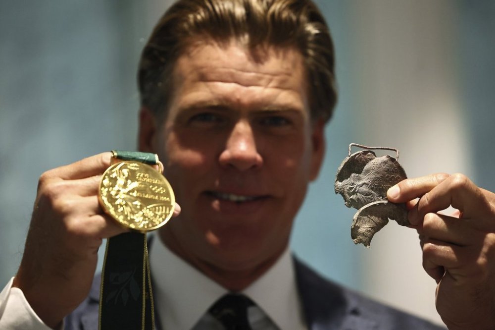 American swimmer Gary Hall Jr. holds an original medal from Atlanta 1996, that melted during the wildfires in Los Angeles that destroyed his home earlier this year, while holding a replica of the Olympic medal that IOC President Thomas Bach presented to him during a ceremony at the Olympic House in Lausanne, Switzerland, Monday, May 5, 2025. (Denis Balibouse/Keystone/Reuters Pool via AP)