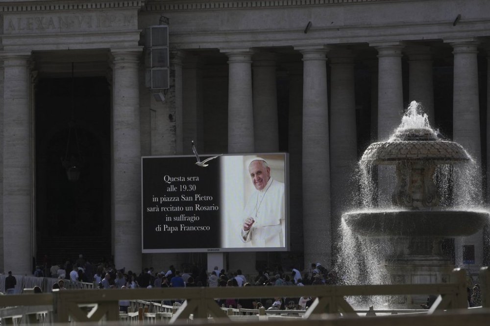People walk in St. Peter's Square at the Vatican as a giant screen reports that a rosary prayer for the late Pope Francis has been scheduled for 19.30, Monday, April 21, 2025. THE CANADIAN PRESS/AP-Alessandra Tarantino