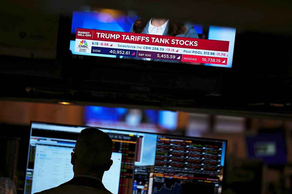 A screen displays financial news as traders work on the floor at the New York Stock Exchange in New York, Thursday, April 3, 2025. (AP Photo/Seth Wenig)