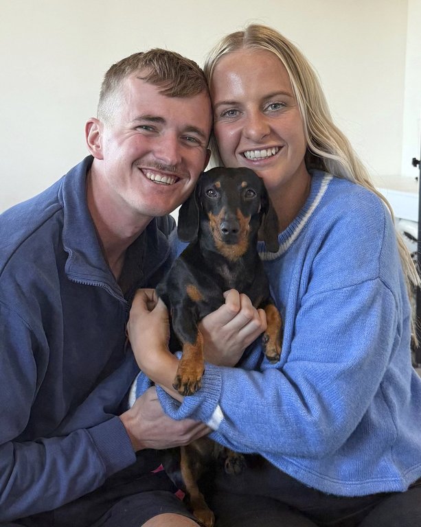 Georgia Gardner and partner Josh Fishlock hold Valerie, their miniature dachshund after being reunited on Kangaroo Island in South Australia after Valerie was missing for 540 days, Tuesday, May 6, 2025. (Ruby Stewart/The Advertiser via AP)