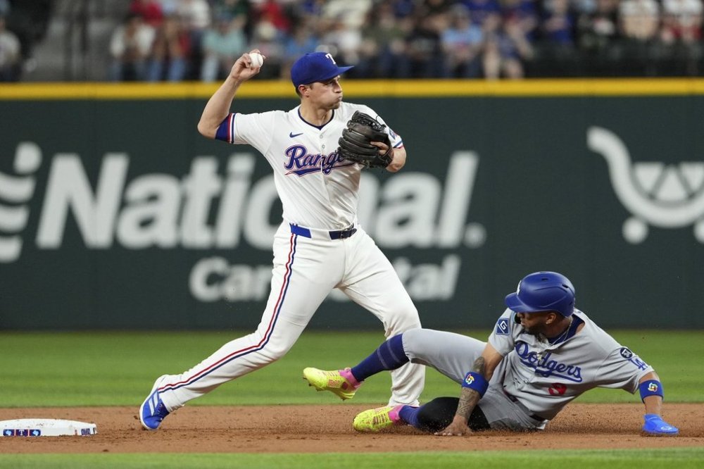 Texas Rangers shortstop Corey Seager, left, throws to first base on a fielder's choice as Los Angeles Dodgers' Eddie Rosario, right, is out at second base during the third inning of a baseball game Saturday, April 19, 2025, in Arlington, Texas. (AP Photo/Jeffrey McWhorter)