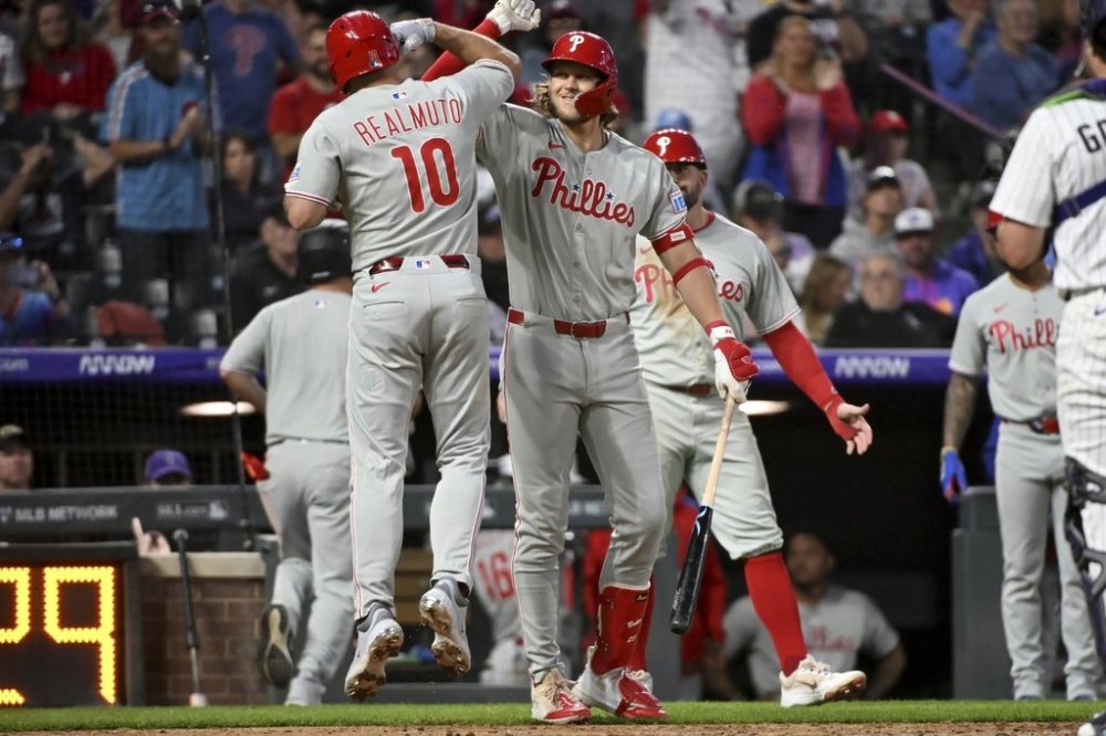 Philadelphia Phillies' J.T. Realmuto (10) and Alec Bohm (28) celebrate after Realmuto's two-run home run in the sixth inning of a baseball game against the Colorado Rockies Wednesday, May 21, 2025, in Denver. (AP Photo/Geneva Heffernan)