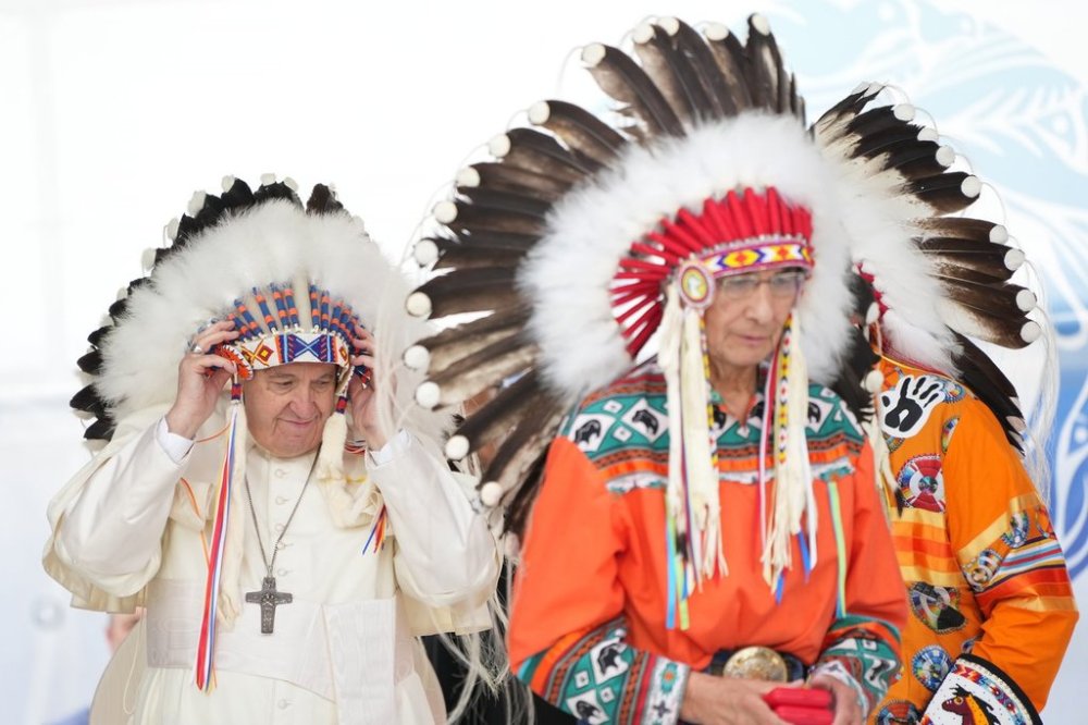 Pope Francis adjusts a traditional headdress he was given after his apology to Indigenous people as Chief Wilton Littlechild looks on during a ceremony in Maskwacis, Alta., as part of his papal visit to Canada on July 25, 2022. THE CANADIAN PRESS/Nathan Denette