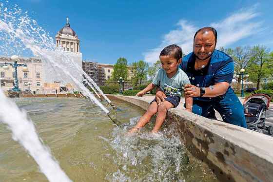 Ansh Poddar, 2, and his father, Chandan, take a moment to enjoy the cool water at the fountain behind the Manitoba Legislative Building on Monday afternoon. (Mike Deal / Free Press)