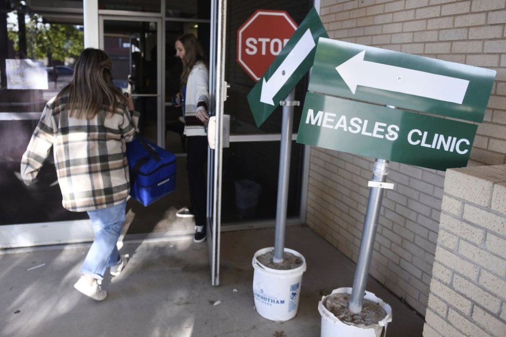 FILE - Health department staff members enter the Andrews County Health Department measles clinic carrying doses of the measles, mumps and rubella vaccine, Tuesday, April 8, 2025, in Andrews, Texas. (AP Photo/Annie Rice, File)