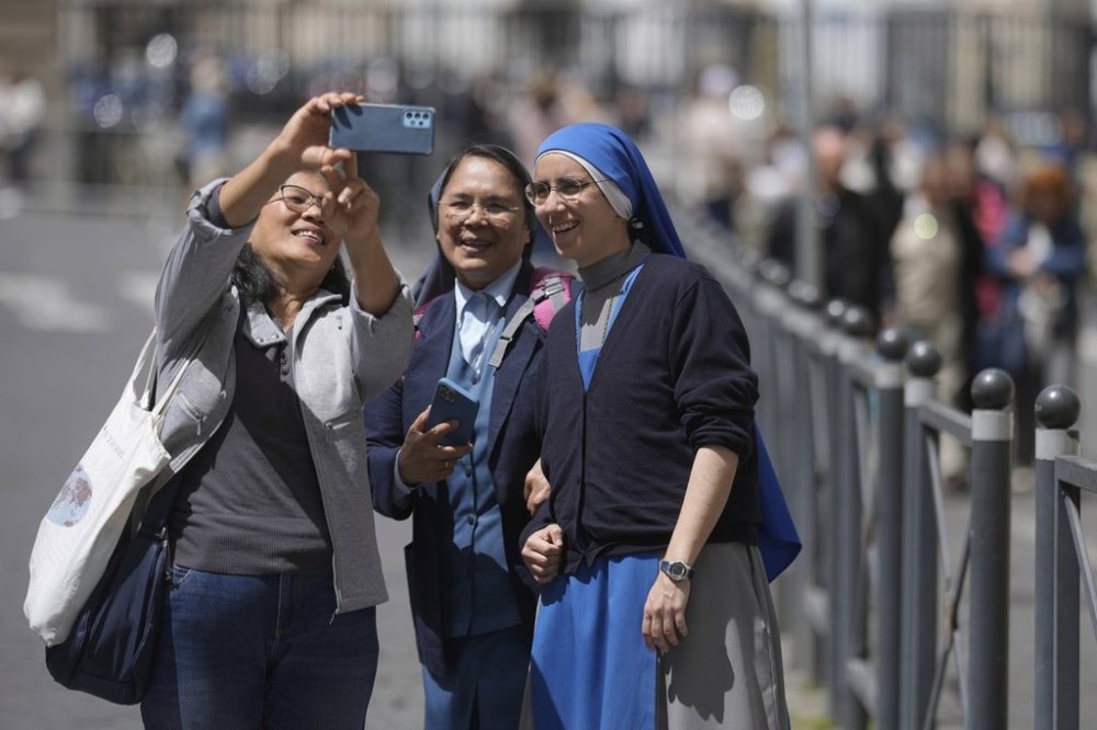 A woman takes selfie with nuns at St. Peter's Square where 133 cardinals are gathering on the second day of the conclave to elect successor of late Pope Francis, at the Vatican, Thursday, May 8, 2025. (AP Photo/Markus Schreiber)