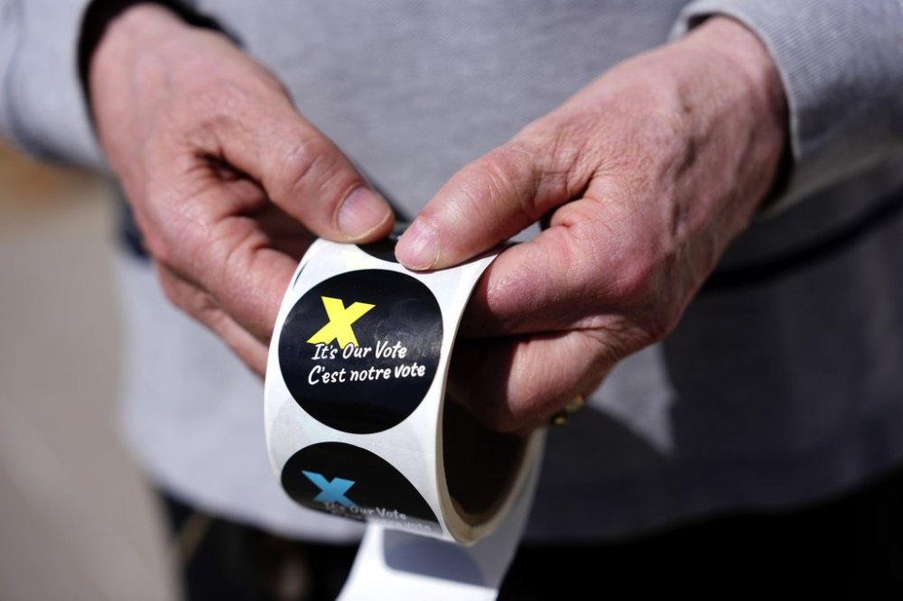A voting information officer holds stickers to be given to voters after casting their ballots outside a polling location in Ottawa on Monday, April 28, 2025. THE CANADIAN PRESS/Justin Tang