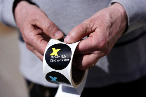 A voting information officer holds stickers to be given to voters after casting their ballots outside a polling location in Ottawa on Monday, April 28, 2025. THE CANADIAN PRESS/Justin Tang