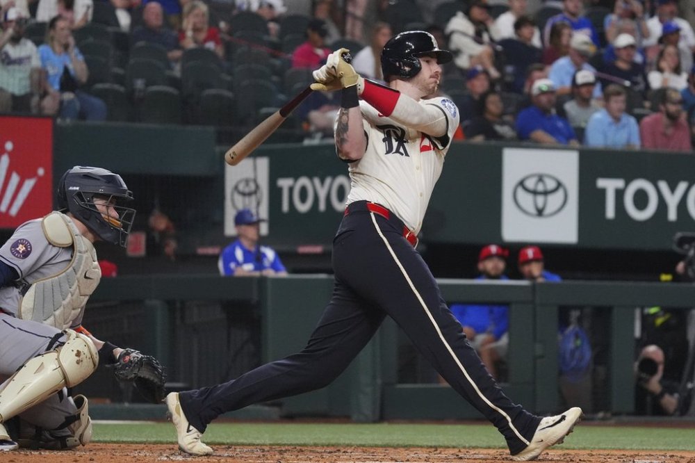 Texas Rangers' Jonah Heim, right, and Houston Astros catcher Victor Caratini, left, watch Heim's single that scored teammates Josh Jung and Evan Carter during the second inning of a baseball game, Friday, May 16, 2025, in Arlington, Texas. (AP Photo/LM Otero)
