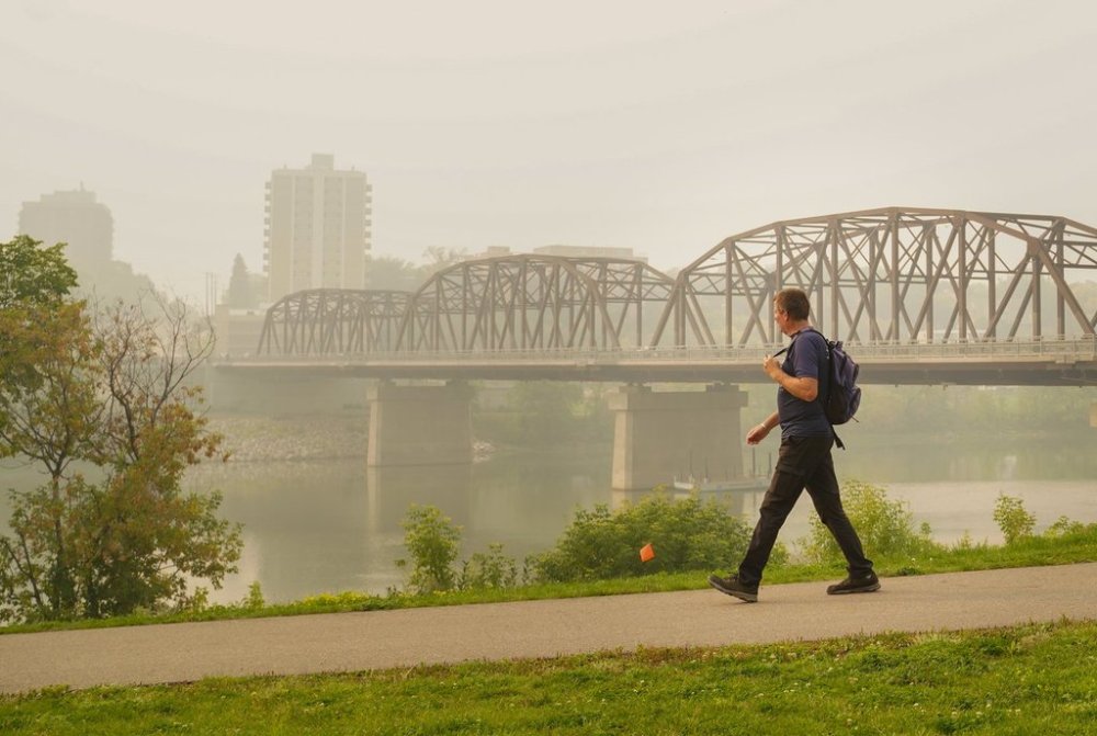 A person walks as the South Saskatchewan River is enveloped by forest fire smoke in Saskatoon, Sask., Sunday, Sept. 3, 2023. THE CANADIAN PRESS/Heywood Yu