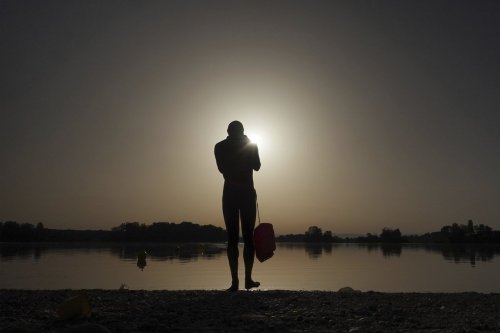 FILE - A man prepares to enter the water as the sun rises above the Miribel lake, outside Lyon, France, June 18, 2022. (AP Photo/Laurent Cipriani, File)