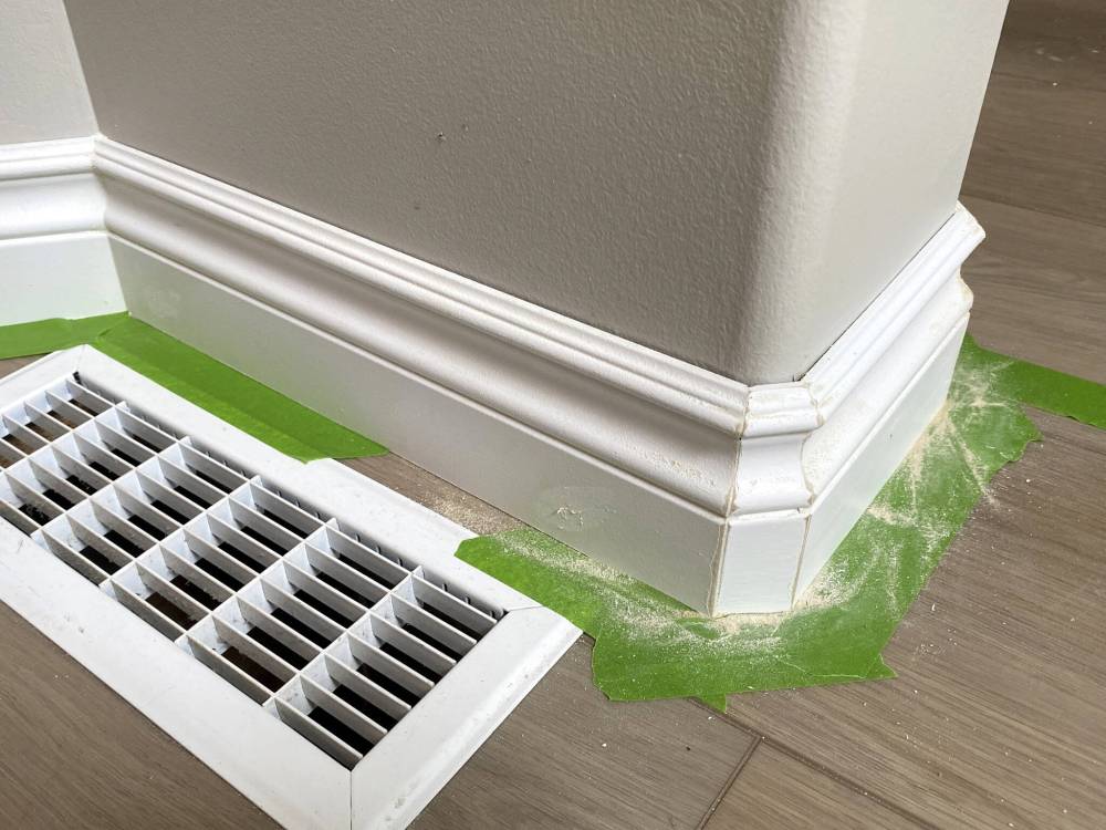Corners of short baseboard sections at every rounded corner bead location are sanded and painted before caulk is added along the top edge.