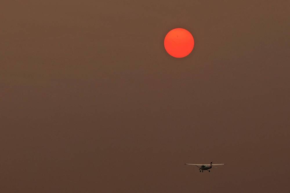 Tim Smith/The Brandon Sun
The sun, obscured by smoke from forest fires in northern Manitoba, glows pink in the sky as an aircraft takes flight at the Brandon Airport.