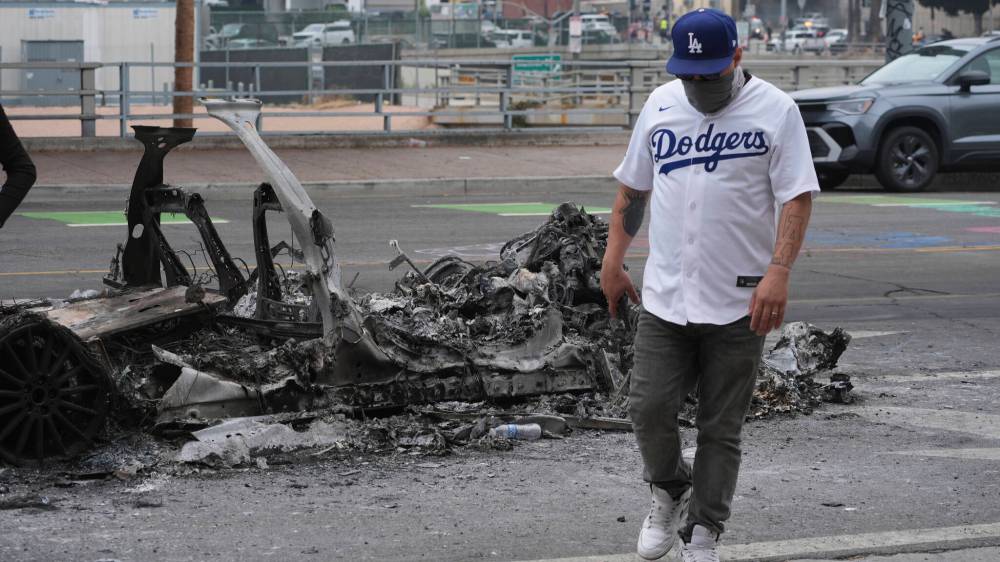 Damian Dovarganes / The Associated Press files
A man walks past a burned-out car after a night of protests in downtown Los Angeles on Monday.