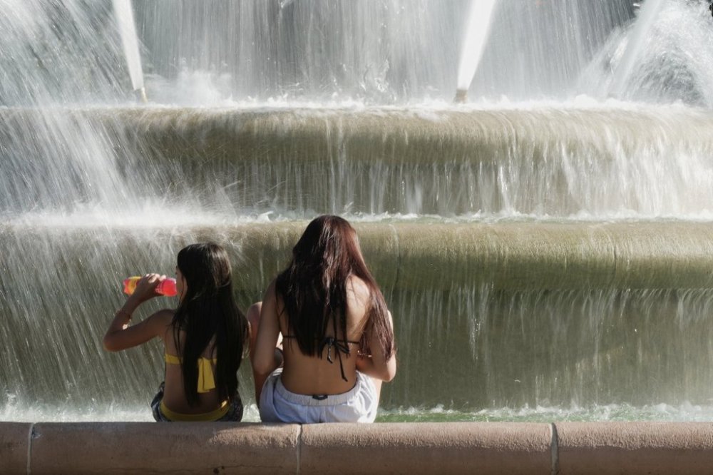 Kids cool off in the mist from a fountain as temperatures approach 100 degrees, Friday, June 20, 2025, in Kansas City, Mo. (AP Photo/Charlie Riedel)