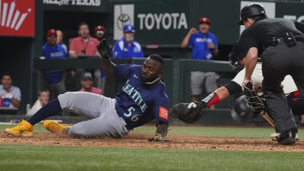 Seattle Mariners' Randy Arozarena (56) scores against Texas Rangers catcher Kyle Higashioka, back right, during the 12th inning of a baseball game, Friday, June 27, 2025, in Arlington, Texas. (AP Photo/LM Otero)