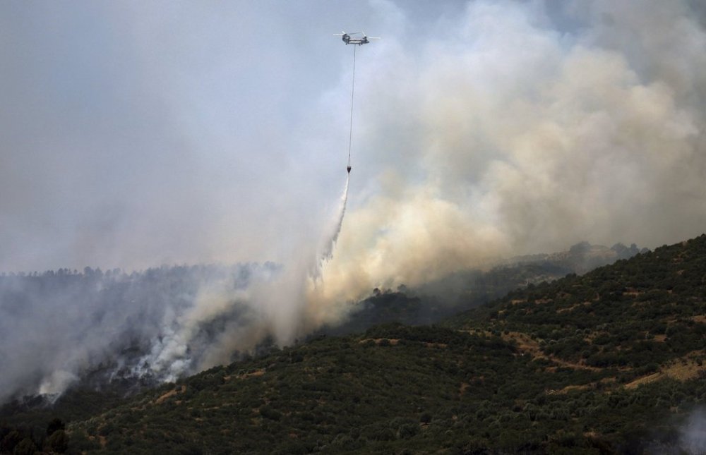 A helicopter drops water to extinguish a fire raging across a forested area in Odemis, near Izmir, Turkey, Friday, July 4, 2025. (Cengiz Malgir/Dia Photo via AP)