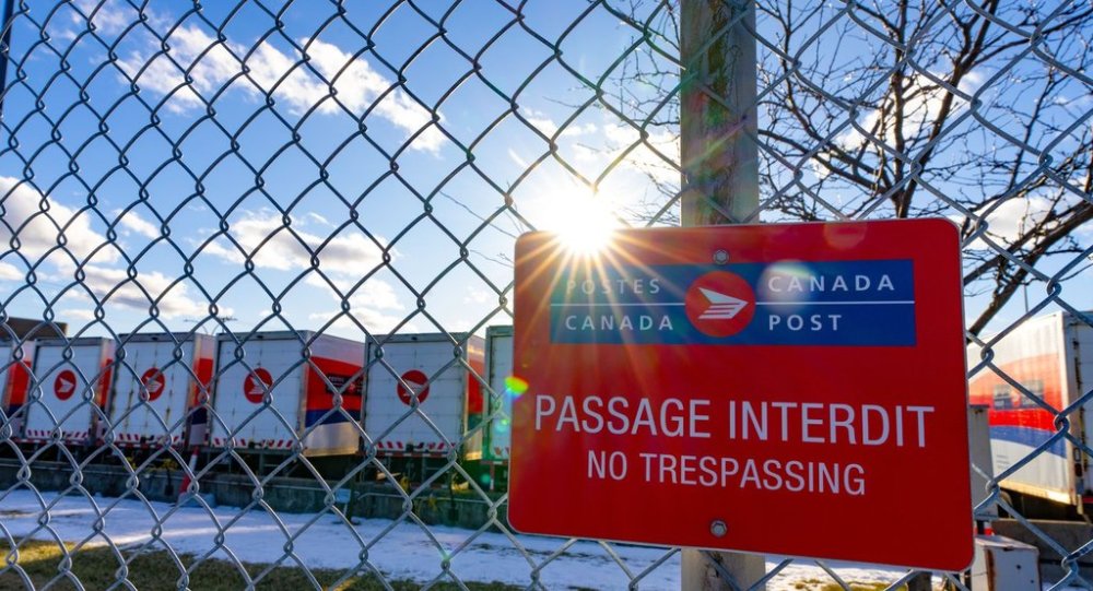 Canada Post trucks are seen behind a fence at a distribution centre in Montreal on Friday, Dec.13, 2024. THE CANADIAN PRESS/Christinne Muschi