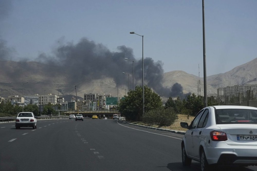 Cars drive on a highway as smoke rises from an oil storage facility after it appeared to have been struck by an Israeli strike on Saturday, in Tehran, Iran, Monday, June 16, 2025. (AP Photo/Vahid Salemi)