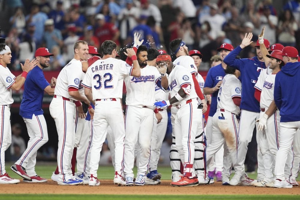 Texas Rangers' Marcus Semien, center with white gloved hand raised, is congratulated by teammates after driving in the winning run in the 10th inning of a baseball game against the Seattle Mariners, Saturday, June 28, 2025, in Arlington, Texas. (AP Photo/Tony Gutierrez)