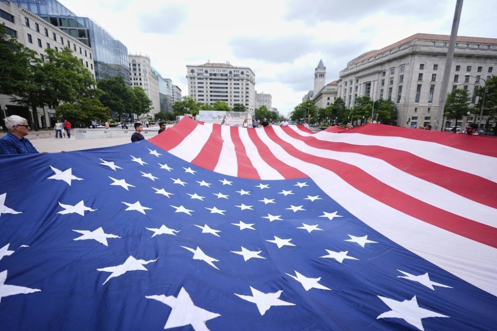 People hold a large American flag at Freedom Plaza before a parade commemorating the Army's 250th anniversary, coinciding with President Donald Trump's 79th birthday, Saturday, June 14, 2025, in Washington. (AP Photo/Manuel Balce Ceneta)