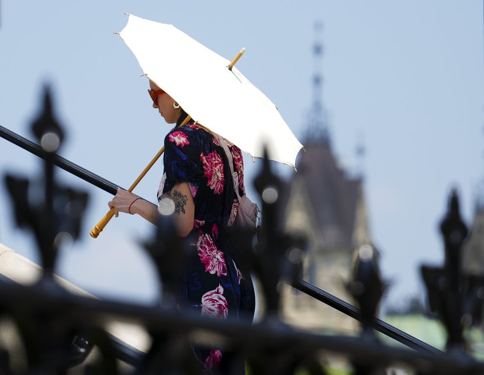 A person carries an umbrella for shade as they walk on Parliament Hill in Ottawa on Tuesday, June 18, 2024. THE CANADIAN PRESS/Sean Kilpatrick