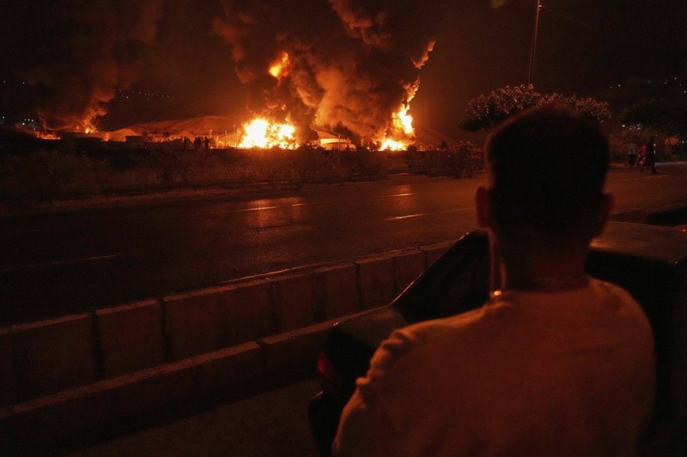 A man looks at flames rising from an oil storage facility after it was hit by an Israeli strike in Tehran, Iran, early Sunday, June 15, 2025. (AP Photo/Vahid Salemi)